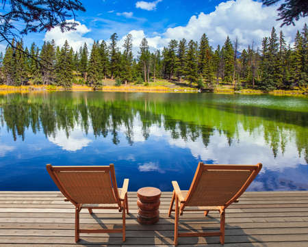 Two wooden sun loungers and a platform for tourists. Round small lake with cold green water. Indian summer. The Rocky Mountains. Travel and photo tourism conceptの写真素材