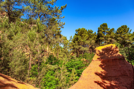 Walk along the most beautiful red-yellow-orange route. The rocks are covered with forest. Sunny and warm day. Bizarre ocher rocks. Provence, France. The village of Roussillon.の写真素材