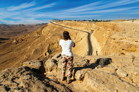 Woman photographing a beautiful landscape on a steep cliff. Israel. Crater Makhtesh Ramon in the Negev Desert declared a Geological Reserve. The morning after the starfall. Israelの写真素材