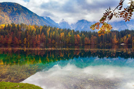Lake Fuzine. Italy. Orange, yellow and red trees are reflected in the green smooth water of the lake. Magnificent colors of autumnの写真素材