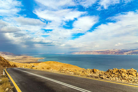 Wonder of nature - the Dead Sea. The highway runs along the coast of the Dead Sea. Cloudy and warm January day. Israel. Jordan on the opposite coast of the sea is illuminated by the dim winter sunの写真素材