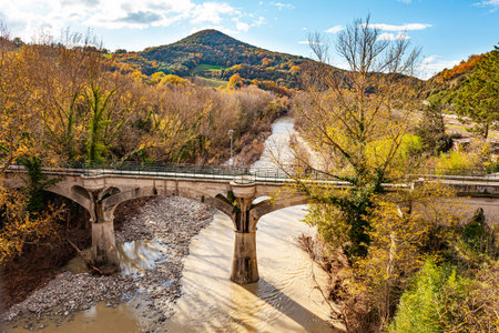 Noon. Beautiful Tuscany. Green, yellow and orange colors of a beautiful Indian summer. Narrow bridge across a small river connects the hilly banksの写真素材
