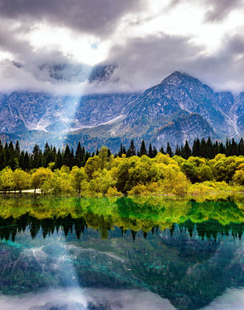 The sun's rays break through the clouds. The lake Fusine in Northern Italy. Mountains covered in mist. The smooth surface of the water reflects forest and mountains. Gorgeous reflections.の写真素材