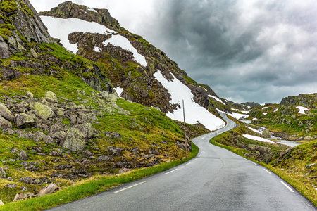 Traveling by camper on road 520. Narrow dangerous mountain road glitters from the rain. Cold July in Norway. Large snowfields remained in the slopes of the mountains.の写真素材