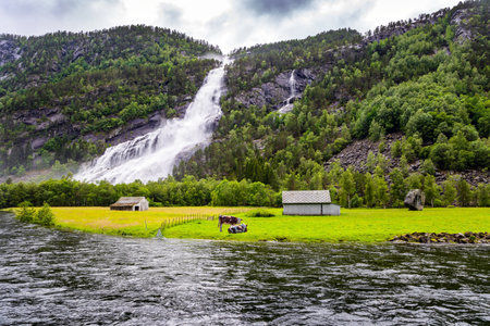Powerful waterfal Vidfossen. Green world of glacial water. Summer, July. White water foam envelops the foot of the waterfall. Incredible Norway.の写真素材