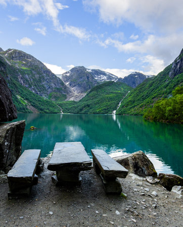 Picturesque mountain lake Bondhuswatnet. Cozy tourist wooden table and benches on the shore. Gorgeous mountainous Norway. Evening soft twilightの写真素材