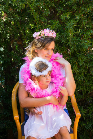 Happy beautiful young mother with a wreath on her head and an adorable little daughter. Background dense evergreen hedge. Concept - portrait and advertising photoの写真素材