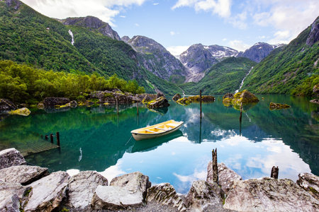 Journey to the fabulous northern country in the summer. Picturesque small boat is moored to the shore. The mountain lake Bondhuswatnet. Evening soft twilight. Norway.の写真素材