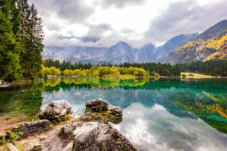 Gorgeous reflections. Picturesque lake Fusine in Northern Italy. Mountains covered in mist. The smooth surface of the water reflects the lush splendor of the surrounding forest and mountains.の写真素材