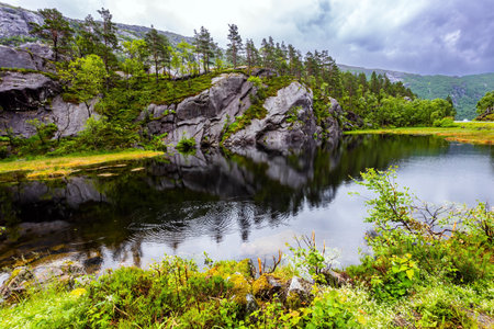 Scenic landscape in Western Norway. Bright reflections of the sky and clouds in the water. Summer cold and rainy day. Quiet small lake next road to Roldalの写真素材