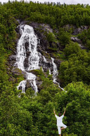 Woman doing yoga. Summer trip to the north of Europe. Vertical rocky waterfall on the most picturesque road in Norway.の写真素材