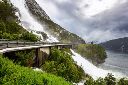 The cascading Langfossen waterfall picturesquely intersects with the highway and flows into the Acre Fjord. Western Norway. Summer cold and rainy day.の写真素材