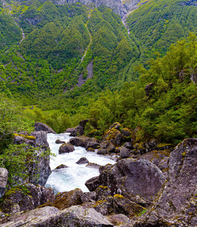 Rumbling turbulent foamy stream of cold water flowing from the lake Bondhuswatnet. Gorgeous mountainous Norway. Emerald green of summer grass.の写真素材