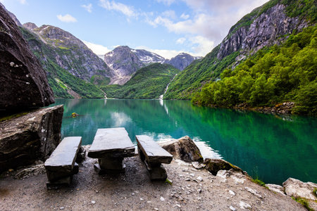 Cozy tourist wooden table and benches on the shore. Picturesque mountain lake Bondhuswatnet. Gorgeous mountainous Norway. Evening soft twilightの写真素材