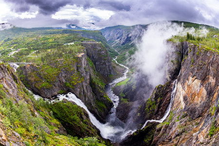 The Hardangerfjord. Voringsfossen is one of the most famous Norwegian cascading waterfalls. The waterfall falls into a narrow deep picturesque gorge. Rainy cold July in Norwayの写真素材