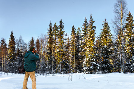 Exotic trip to the Arctic. Tourist with a photo bag photographs of the winter forest. Sunset in the  coniferous forest. Travel to Lapland. The sun is low on the horizon.の写真素材