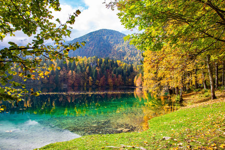 Sunrise. Lake Fusine in northern Italy. The smooth surface of the water reflects the lush splendor of the surrounding forests and mountains.  Mountains covered in morning mistの写真素材