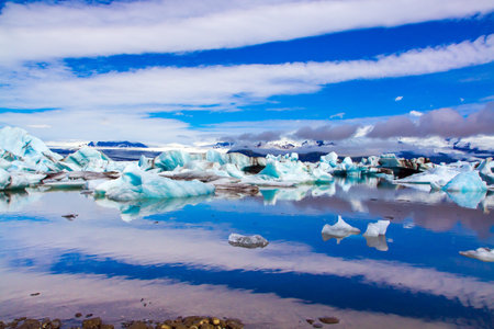 Clouds reflected in the smooth water of the largest glacial lagoon Jokulsaurloun. Iceland. Cold early summer morning. White and blue icebergs and ice floes. The concept of northern and photo tourismの写真素材