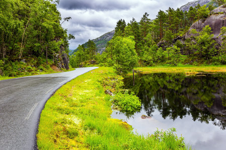 The picturesque road in Norway. Quiet small lake next to the road. Summer trip to the north of Europe. Summer cold and rainy day. Western Norway.の写真素材