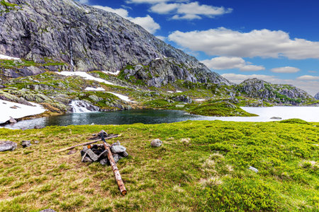 Remains of a campfire by the lake. Cold summer in Norway. Traveling by camper on road 520. Large snowfields is reflected in the water of the lake.の写真素材