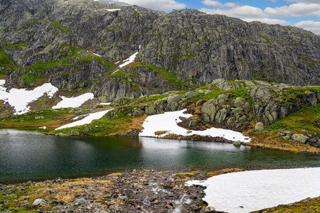 Cold summer in Norway. Traveling by camper on road 520. Gray rocks surround the lake. Large snowfields is reflected in the water of the lake.の写真素材
