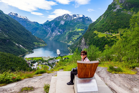 The famous Queen Sonja chair. Elderly woman is relaxing in this chair. The largest Norwegian fjord Geiranger. Summer trip to Norway.の写真素材