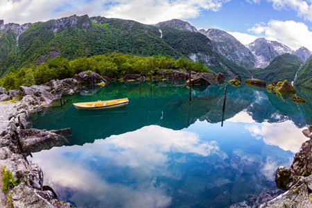 Picturesque small boat is moored not far from the shore. Emerald green of summer grass. The mountain lake Bondhuswatnet. The picture was taken with a fisheye lens. Gorgeous Norway.の写真素材