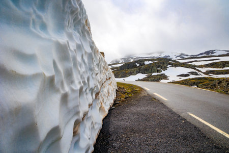 Multi-meter wall of snow along the road. Great asphalt "Snow Road". Cold July in Northern Europe. Low gray clouds and fog. Journey to the fabulous northern country of Norway. "Bjorgavegen"の写真素材