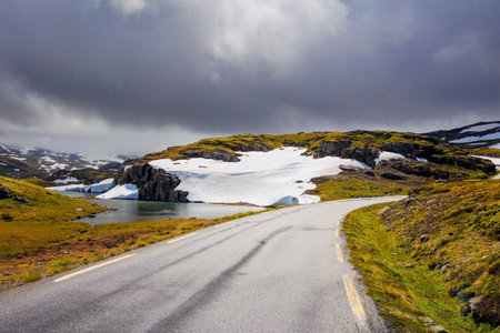 Scenic ice landscape of northern Norway. Cold snowy frosty July. Heavy dark clouds hung over great "Snow Road". Huge cold snowfields and sharp stone placers. "Bjorgavegen"の写真素材