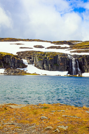 Incredible trip to the north of Norway. Cold July. Scenic ice landscape of northern Norway. Tall Flotane waterfall falls into the lake. Snow road.の写真素材