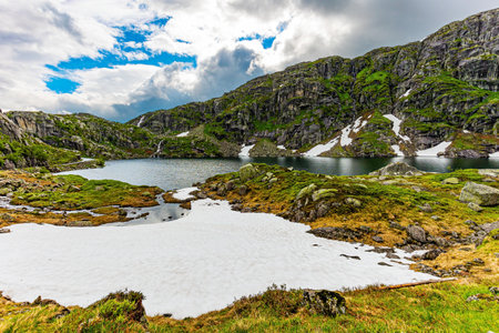 Large snowfields remained in the lowlands and on the slopes of the mountains. Ice lake surrounded by green mountains. Traveling on road 520. Cold summer in Norway.の写真素材