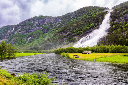 Powerful waterfal Vidfossen. Green world of glacial water. Summer, July. White water foam envelops the foot of the waterfall. Incredible Norway.の写真素材