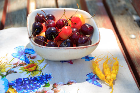 Spring has come to Israel. Large yellow and dark red cherries in ceramic vase. Linen napkin with floral pattern. Warm sunny dayの写真素材