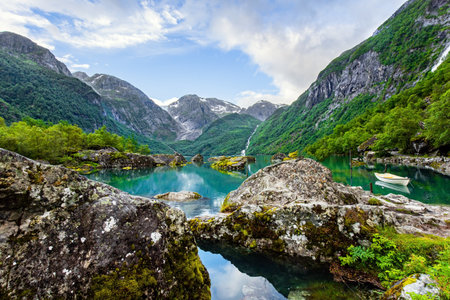 Journey to the fabulous northern country in the middle of summer. Picturesque small boat is moored to the shore. The mountain lake Bondhuswatnet. Evening soft twilight. Norway.の写真素材