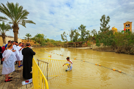 QASR EL YAHUD, ISRAEL - MARCH 2, 2020: Woman in baptismal shirt comes out of the water. The priest conducts the rite of baptism. The site of the baptism of Jesus Christ in a historical place on the Jordan River.のeditorial素材