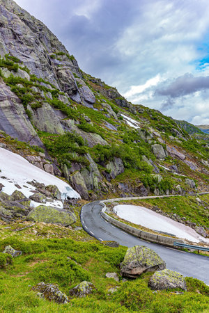Narrow winding mountain road. Green rocks surround the lake. Snowfields remained in the slopes of the mountains. Traveling by camper on road 520. Cold July in Norway.の写真素材