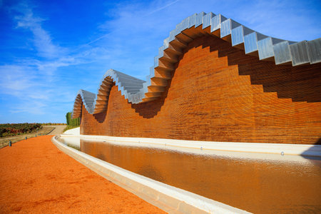 Wave-shaped winery roof. Fragment of the facade is reflected in the pool. Winery - bodega Bodegas Ysios. Journey to the warm Spanish autumn. The sunset.の写真素材