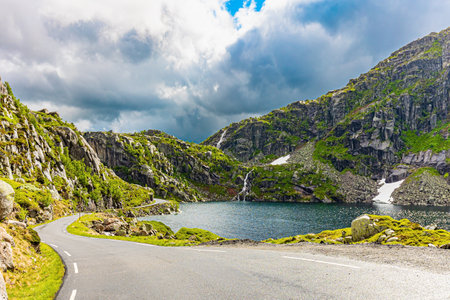 Traveling by camper on road 520. Narrow dangerous mountain road. Cold July in Norway. Large snowfields remained in the slopes of the mountains. Gray rocks surround the lake.の写真素材