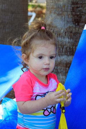 Adorable little girl playing on the beach in the shade of palm trees. Happy family. Family vacation in a hotel on the Greek island of Cyprus. Cozy beach on the Mediterranean coast.の写真素材