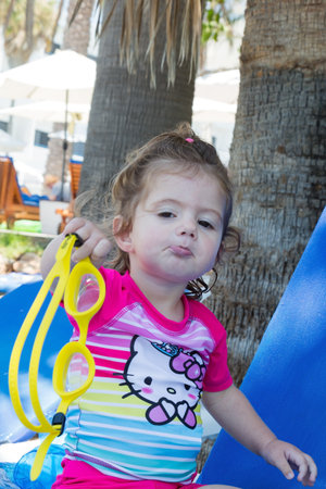 Charming little girl playing on the beach in the shade of palm trees. Cozy beach on the Mediterranean coast. Family vacation in a hotel on Cyprus.の写真素材