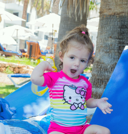The little girl playing on the beach in the shade of palm trees. Cozy beach on the Mediterranean coast. Family vacation in a hotel on the Greek island of Cyprus.の写真素材