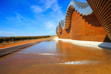 Fragment of the facade is reflected in the pool. Winery - bodega Bodegas Ysios. Bright flaming colors of the sunset. Journey to the warm Spanish autumn. Laguardiaの写真素材