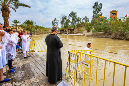 QASR El-YAHUD, ISRAEL - MARCH 2, 2020: Baptism ceremony. Man in baptismal shirt enters the water of the Jordan River. The site of the baptism of Jesus Christ. The concept of religious tourismのeditorial素材