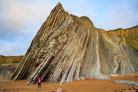 Woman in a red jacket photographs Playa Zumaya. Low tide in the Atlantic. Flysch - unique landscape of underwater rocks exposed at low tide. The Basque Country - Itsurun.の写真素材