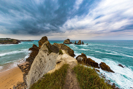 Cliffs and huge stones oppose the ocean. Spanish coast, Cantabria. Rocky coastline of the Atlantic Ocean. Stormy autumn day in the Bay of Biscay. Portio beach.の写真素材