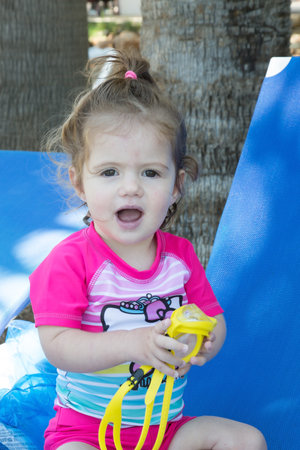 Charming little girl playing on the beach in the shade of palm trees. Happy family. Family vacation in a hotel on the Greek island of Cyprus. Cozy beach on the Mediterranean coast.の写真素材