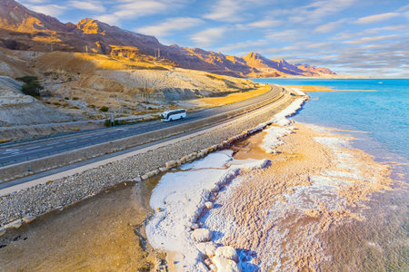 Asphalt highway runs along the seashore. Dead Sea, Israel. Shallowed Dead Sea photographed from a drone. Evaporated salt was deposited along the shore. Evening twilight in winterの写真素材
