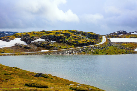 "Snow Road" in Norway. The cold water of the lake is covered with ice floes. Incredible trip to the north of Norway in cold July. Hills and valleys are covered with non-melting snowfieldsの写真素材