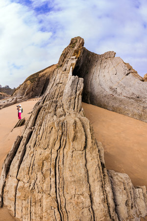 Woman in pink pants photographing a stunning landscape. Incredible rock formations, stones and boulders. Adorable sea gull. Cantabria, Spain. The Playa de la Arnia beach.の写真素材