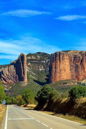Asphalt highway passes through the rocks. Part of the foothills of the Pyrenees. The Mallets of Riglos. Hoya de Huesca, Aragon. Hot sunny afternoon. Romantic trip to Spain.の写真素材